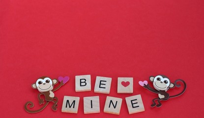 two monkeys holding pink hearts with block letters be mine on a red background with writing space