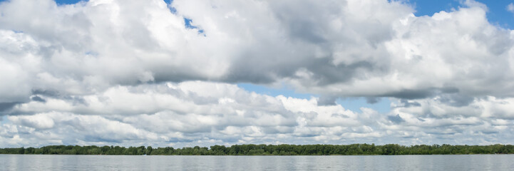 Obraz na płótnie Canvas Big white clouds on the blue sky above the river.