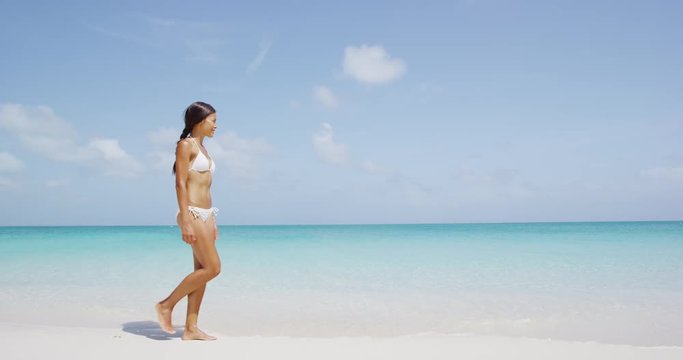 Woman walking in bikini on beach on travel vacation.