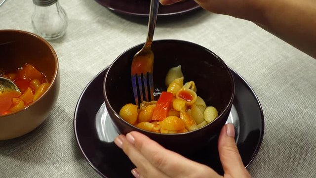 Young woman eats a plate with pasta. On the table lecho sauce made from sweet peppers.
