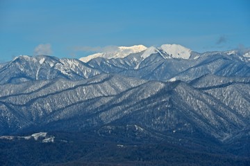 Panorama of snowy mountains. Winter forest and rocky peaks in the snow. Sunny winter day.