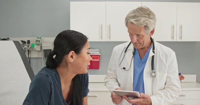 Doctor listening to medical history from patient in exam room with tablet
