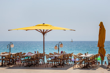 Yellow umbrellas and cafe tables line the Menton promenade facing the beach