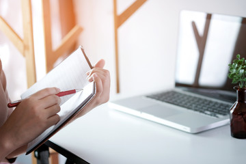 young woman studying while sitting at the table with laptop computer and notebook during lesson in classroom.