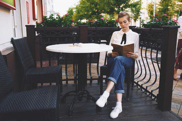 business woman with a book sits at a table on the veranda outside