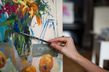 A young woman artist paints a picture in oil on the easel. Selective focus.