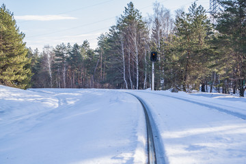 Railway semaphore in winter green pine forest. Blue sky and clouds. Morning in the winter forest. WInter forest landscape with railway.