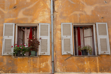 Fototapeta na wymiar White shuttered windows in an old crumbling yellow wall in Menton, south eastern France