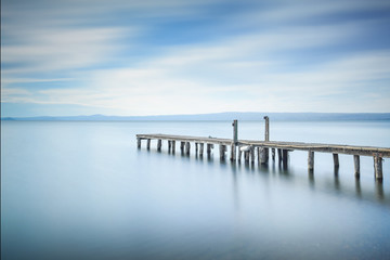 Wooden pier or jetty remains on a blue lake. Long Exposure.