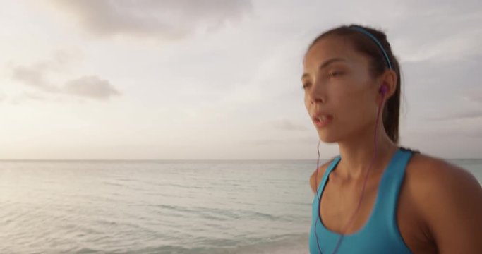 Athlete running woman runner listening to music on her phone using earphones on summer beach. Fitness sport girl jogging fast training cardio. STEADICAM SLOW MOTION, RED EPIC.