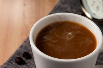 Hot coffee in white cup and coffee beans, on brown cloth at put on the table