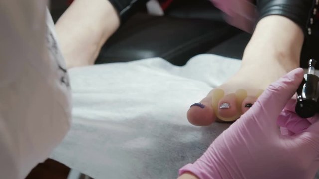 Manicurist in pink, the hygienic gloves paint a black nail Polish at the foot of a client at the salon. The concept of beauty