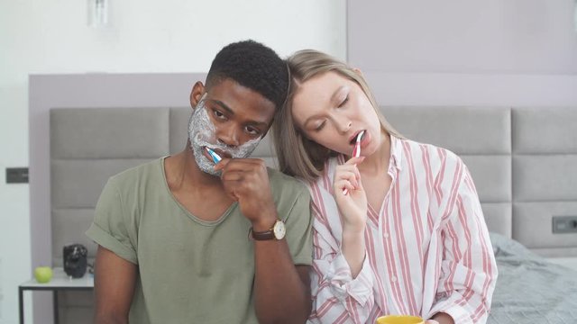 Multiethnic sleepy couple, sitting close, brushing teeth in morning, daily routine dental care.