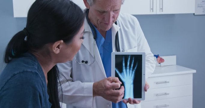 Doctor using tablet computer with x-ray of hand explaining arthritis to patient