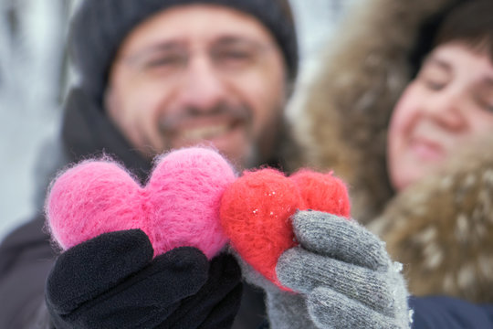 Happy middle-aged couple holding in hands two woolen hearts outdoors