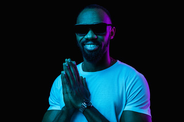 The retro wave or synth wave portrait of a young happy smiling african man in sunglasses at studio. High Fashion male model in colorful bright neon lights posing on black background. Art design