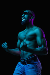 Fototapeta na wymiar Retro or synth wave portrait of a young naked happy screaming african man in sunglasses at studio. High Fashion male model in colorful bright neon lights posing on black background as winner