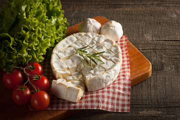 Camembert and brie cheese on wooden background with tomatoes, letuce and garlic. Italian food. Dairy products.