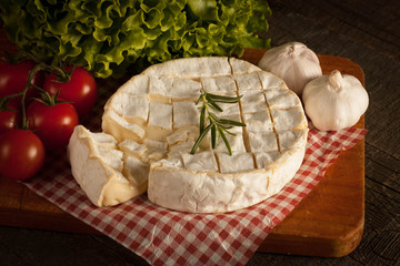 Camembert and brie cheese on wooden background with tomatoes, letuce and garlic. Italian food. Dairy products.