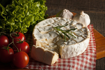 Camembert and brie cheese on wooden background with tomatoes, letuce and garlic. Italian food. Dairy products.