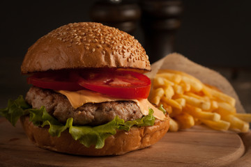 Home made hamburger with beef, onion, tomato, lettuce and cheese. Fresh burger close up on wooden rustic table with potato fries, beer and chips. Cheeseburger.