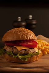 Home made hamburger with beef, onion, tomato, lettuce and cheese. Fresh burger close up on wooden rustic table with potato fries, beer and chips. Cheeseburger.