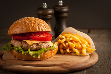 Home made hamburger with beef, onion, tomato, lettuce and cheese. Fresh burger close up on wooden rustic table with potato fries, beer and chips. Cheeseburger.