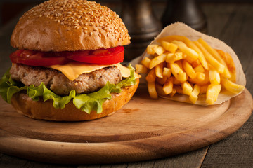 Home made hamburger with beef, onion, tomato, lettuce and cheese. Fresh burger close up on wooden rustic table with potato fries, beer and chips. Cheeseburger.