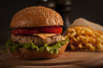Home made hamburger with beef, onion, tomato, lettuce and cheese. Fresh burger close up on wooden rustic table with potato fries, beer and chips. Cheeseburger.