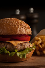 Home made hamburger with beef, onion, tomato, lettuce and cheese. Fresh burger close up on wooden rustic table with potato fries, beer and chips. Cheeseburger.