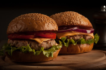 Home made hamburger with beef, onion, tomato, lettuce and cheese. Fresh burger close up on wooden rustic table with potato fries, beer and chips. Cheeseburger.