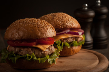 Home made hamburger with beef, onion, tomato, lettuce and cheese. Fresh burger close up on wooden rustic table with potato fries, beer and chips. Cheeseburger.