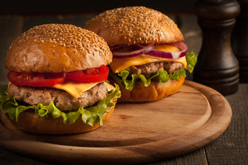 Home made hamburger with beef, onion, tomato, lettuce and cheese. Fresh burger close up on wooden rustic table with potato fries, beer and chips. Cheeseburger.