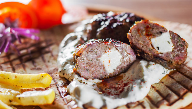Spicy bifteki, frikadelle or frikkadel meatballs with minced beef and lamb with pita bread, tzatziki dip, vegetables salad and French fries. Greek meatballs keftedes or Keftedakia with feta