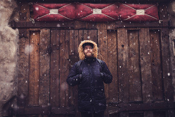 Young bearded guy in winter coat standing near wood background