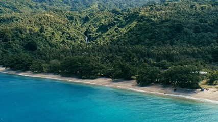 aerial drone image of a south pacific village on a remote island with sandy beach shore and lush...