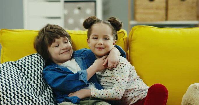 Lovely small kids, boy and girl, hugging and laughing on the yellow couch at home. Sister and brother love.
