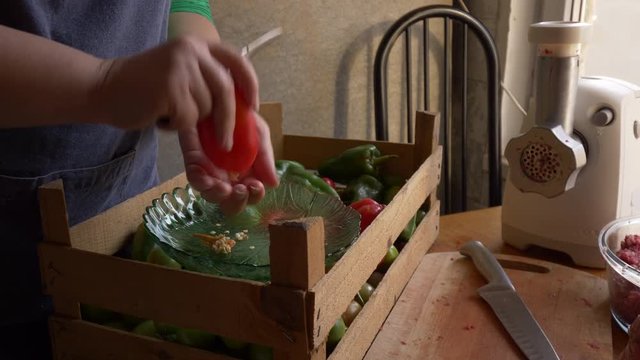 Female cook in an apron with is preparing a sweet pepper stuffed with meat in kitchen. Girl fills peppers with minced meat and puts in pan for cooking.