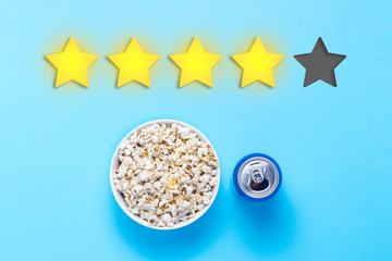 Bowl of popcorn and can with drink on a blue background. Added four stars rating. Reputation. Concept of watching movies, TV shows, sports. Audit and evaluation. Flat lay, top view.