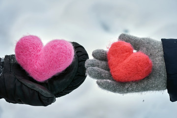 Man and a woman wearing winter gloves giving their woolen hearts to each other on the snow background in winter outdoors. Exchange of hearts. Love, helthcare, devotion,valentine's day concept.