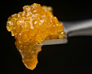 Cannabis concentrate sugar wax dripping off dabbing tool on black background