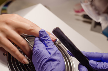 Closeup shot of master in rubber gloves applying a nail file in the beauty salon. Perfect nails manicure process
