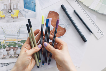 Interior designer holding a color liners, markers, pens. Project drawing and paint tools on work table.