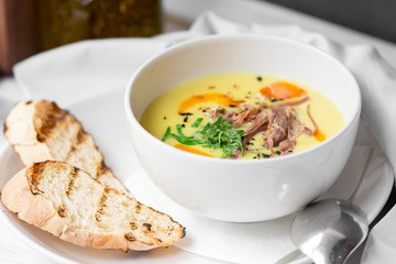 Corn soup puree with toast in white bowl on white wooden background