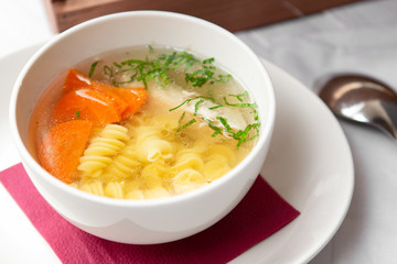 Chicken soup with pasta fusilli in the bowl on the wood table