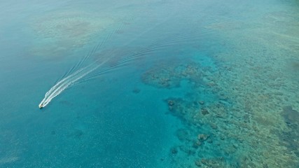 stunning aerial drone image of a a small fishing boat entering an a sea ocean anchorage in a channel next to a coral reef in crystal clear azure blue water at a remote isolated tropical island