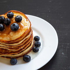 Pancakes with blueberries and honey over black surface, side view. Close-up.