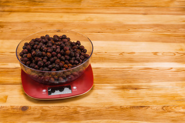 Dry hips in bowl on an electronic scale on a natural wood background with copy space