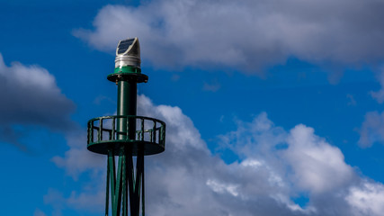 Close up view of green lighthouse lamp. Blue sky with clouds in the background.