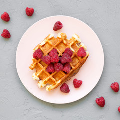 Traditional belgian waffle with raspberries on pink plate over gray background, top view. Flat lay, from above. Close-up.